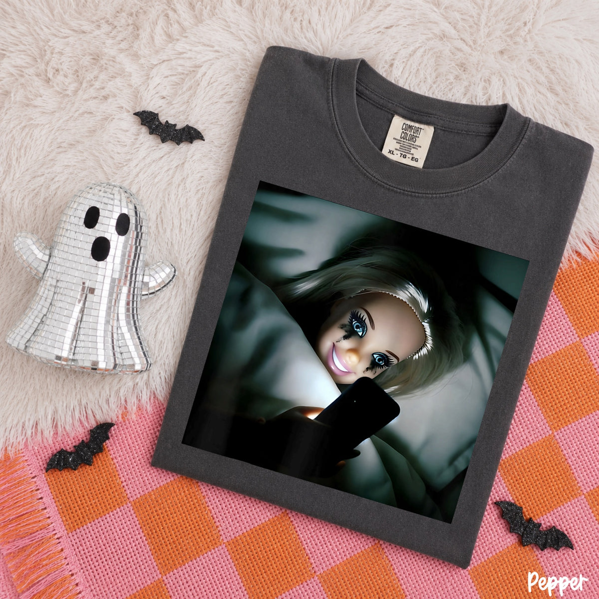 Comfort Colors Pepper T-shirt mockup featuring a doll scrolling on her phone in bed
