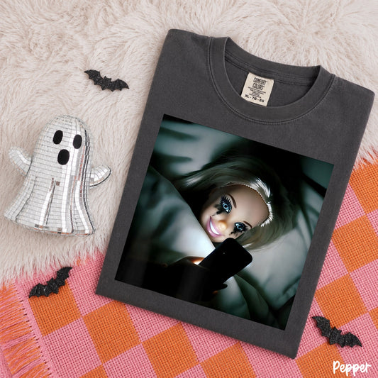 Comfort Colors Pepper T-shirt mockup featuring a doll scrolling on her phone in bed